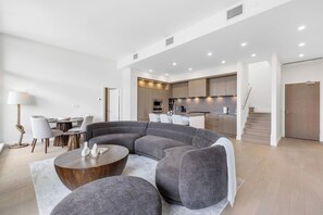 A modern living room with a curved grey sofa, a wooden coffee table, and a dining area with chairs and a lamp.