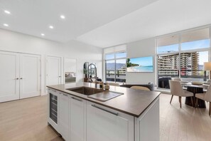 A modern kitchen with a large island, white cabinetry, and a view of a beach and high-rise buildings.