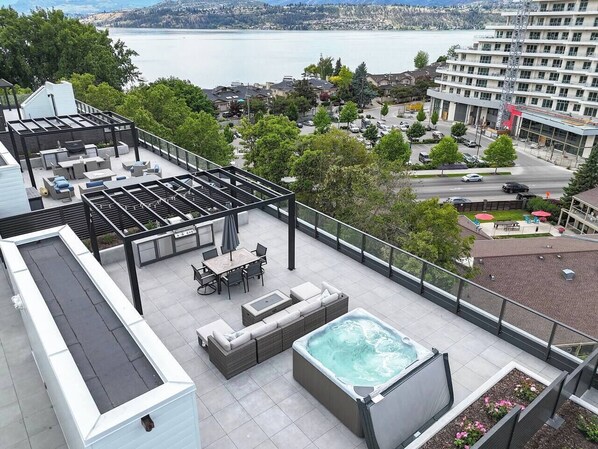 A rooftop terrace with a hot tub, seating area, and a view of a lake and cityscape.