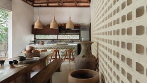 A kitchen with a thatched roof, wooden stools, a large vase, and a patterned wall. - Jungle Villa - Retreats - Pool - Yoga (Tulum)