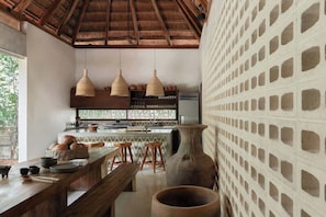 A kitchen with a thatched roof, wooden stools, a large vase, and a patterned wall. - Jungle Villa - Retreats - Pool - Yoga (Tulum)
