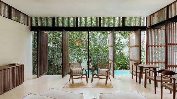 A spacious room with a large sliding glass door leading to a garden, wooden furniture, and a small table with a book. - Jungle Villa - Retreats - Pool - Yoga (Tulum)