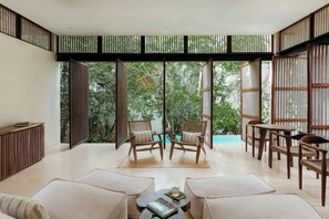 Amplia habitación con un gran ventanal corredero que da a un jardín, muebles de madera y una pequeña mesa con un libro.