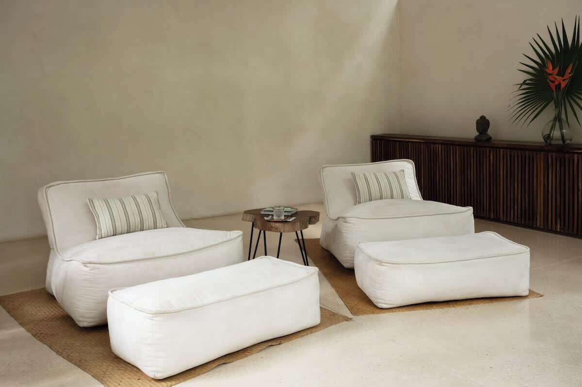 A modern living room with a sofa set, ottomans, a small round table, and a decorative plant.