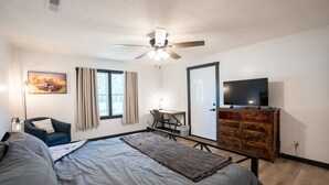Une chambre à coucher comprenant un lit, un bureau, une chaise, un téléviseur et un ventilateur de plafond.