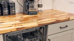 Un lave-vaisselle ouvert, avec un plan de travail en bois au-dessus, une machine à café et une boîte de café espresso.
