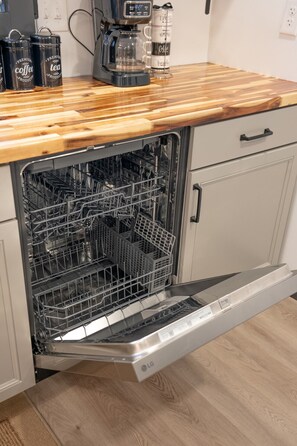 An open dishwasher with a wooden countertop above it, a coffee maker, and a can of espresso. - Whiskey Trails Hollow (Manchester)