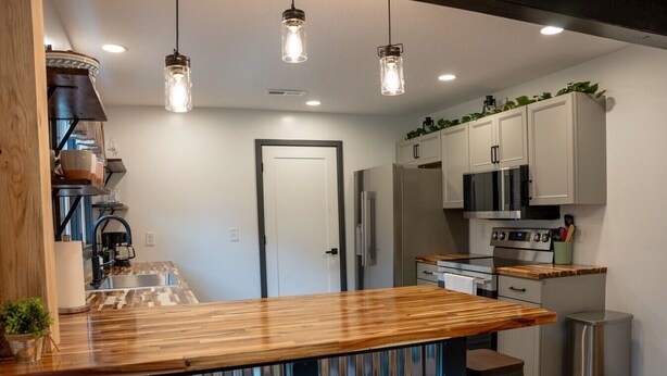 Une cuisine moderne avec un bar en bois, des appareils en acier inoxydable et des luminaires suspendus.