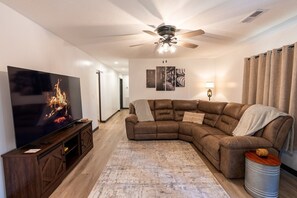 A living room with a sectional sofa, a flat-screen TV, a ceiling fan, and a patterned rug. - Whiskey Trails Hollow (Manchester)