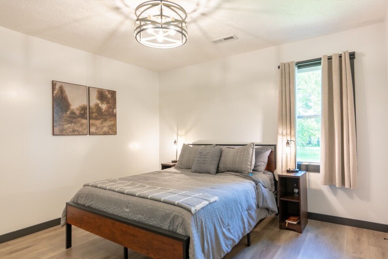 A bedroom with a bed, bedside tables, a ceiling light fixture, and a window with curtains.