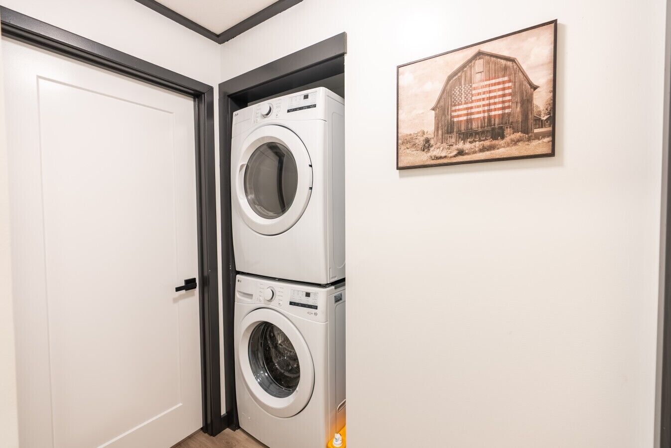 A laundry room with stacked washers and dryers, a door, and a barn-themed wall art.