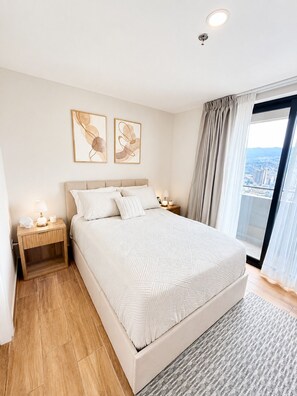 Een slaapkamer met een groot bed, twee nachtkastjes, stadszicht en kunst aan de muur.