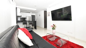 A modern living room with a black sofa, a red rug, a glass coffee table, and a flat-screen TV mounted on the wall. - Stylish 12th Floor Apartment in the Heart of El Peñón (Cali)
