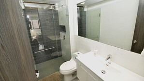 A modern bathroom with a glass-enclosed shower, a white toilet, and a large mirror above the sink. - Stylish 12th Floor Apartment in the Heart of El Peñón (Cali)