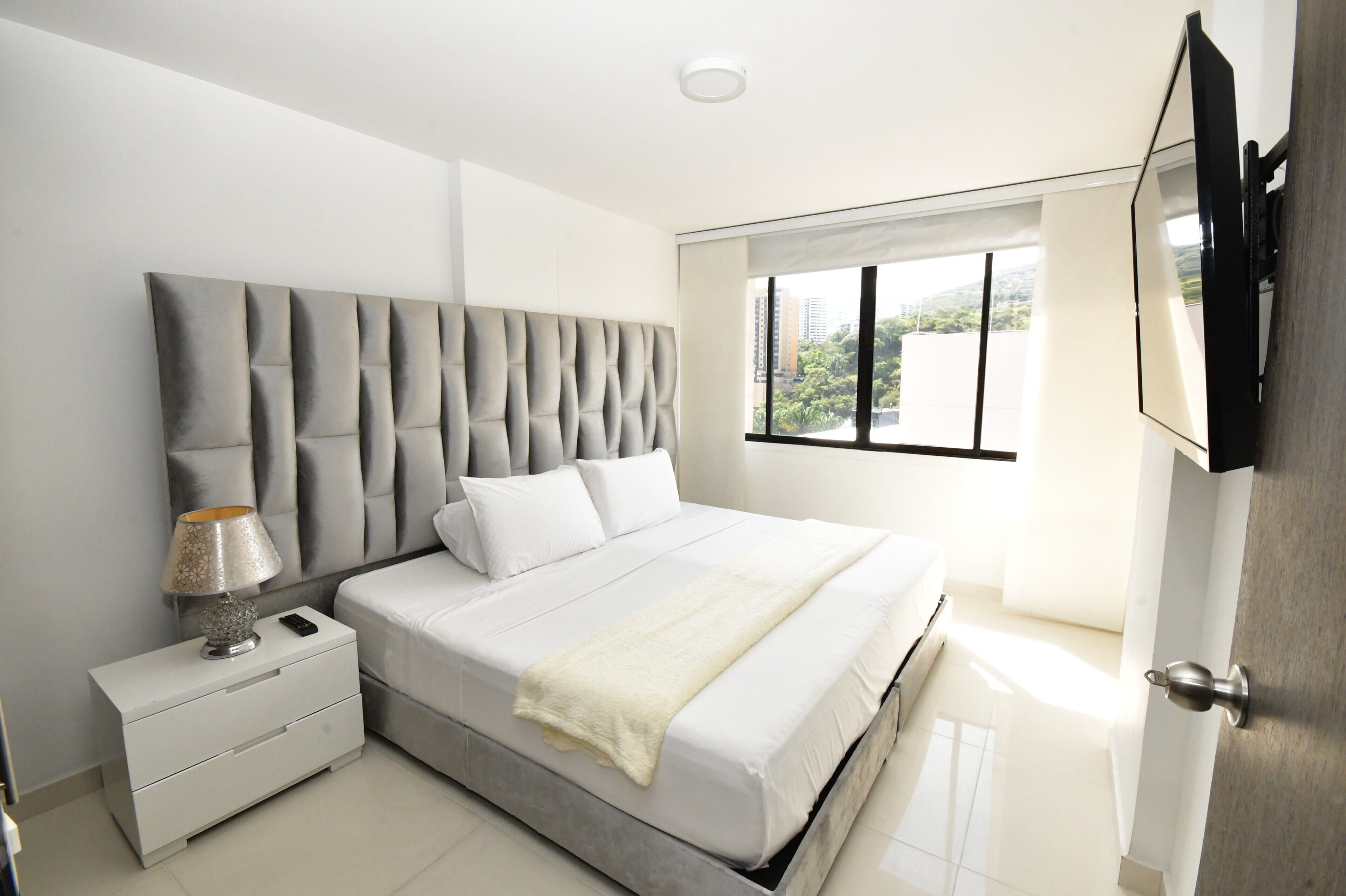 Un dormitorio moderno con una cama grande, una mesita de noche, una lámpara y un televisor montado en la pared.