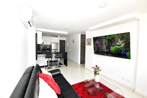 Una sala de estar moderna con un sofá negro, un tapete rojo y un televisor de pantalla plana en la pared.