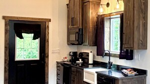 A kitchen with wooden cabinets, a built-in oven, and a window with curtains. - Bungalow with Hot Tub in Birch Tree (Birch Tree)