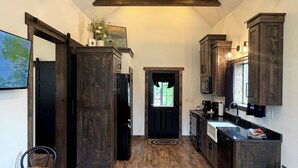 A modern kitchen with dark wood cabinets, a black refrigerator, and a dining area with a wooden table and chairs. - Bungalow with Hot Tub in Birch Tree (Birch Tree)