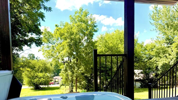 A hot tub with a wooden deck and a view of trees and a house in the background. - Bungalow with Hot Tub in Birch Tree (Birch Tree)