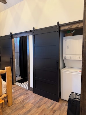 A laundry room with a white washing machine, a black sliding door, and a wooden bench.
