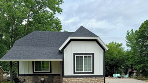 A single-story house with a stone foundation, a dark shingled roof, and a front porch with outdoor seating. - Bungalow with Hot Tub in Birch Tree (Birch Tree)