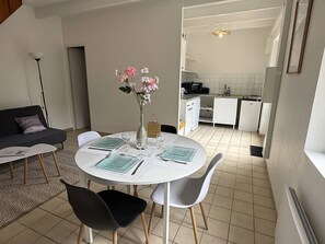 Ein modernes Wohnzimmer mit einem runden Esstisch für vier Personen, einer Couch, einer Vase mit Blumen und einer Küche im Hintergrund.