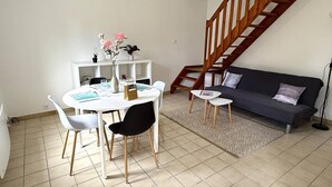 A living room with a dining table, chairs, a sofa, a staircase, and a patterned rug. - NEW LISTING, Domaine de KER-PAULT, between St Cast and Matignon, 3-room cottage 5 minutes from... (MATIGNON)
