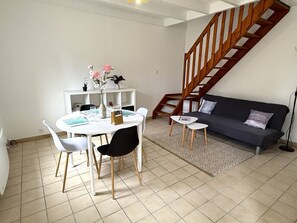 Ein Wohnzimmer mit Esstisch, Stühlen, einer Couch, einer Treppe und einem gemusterten Teppich.