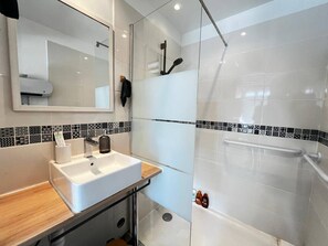 Uma casa de banho moderna com uma pia branca, espelho, chuveiro com porta de vidro e azulejos estampados.