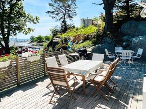 Un patio exterior con mesa y sillas, con vista a un puerto deportivo y un paisaje rocoso.