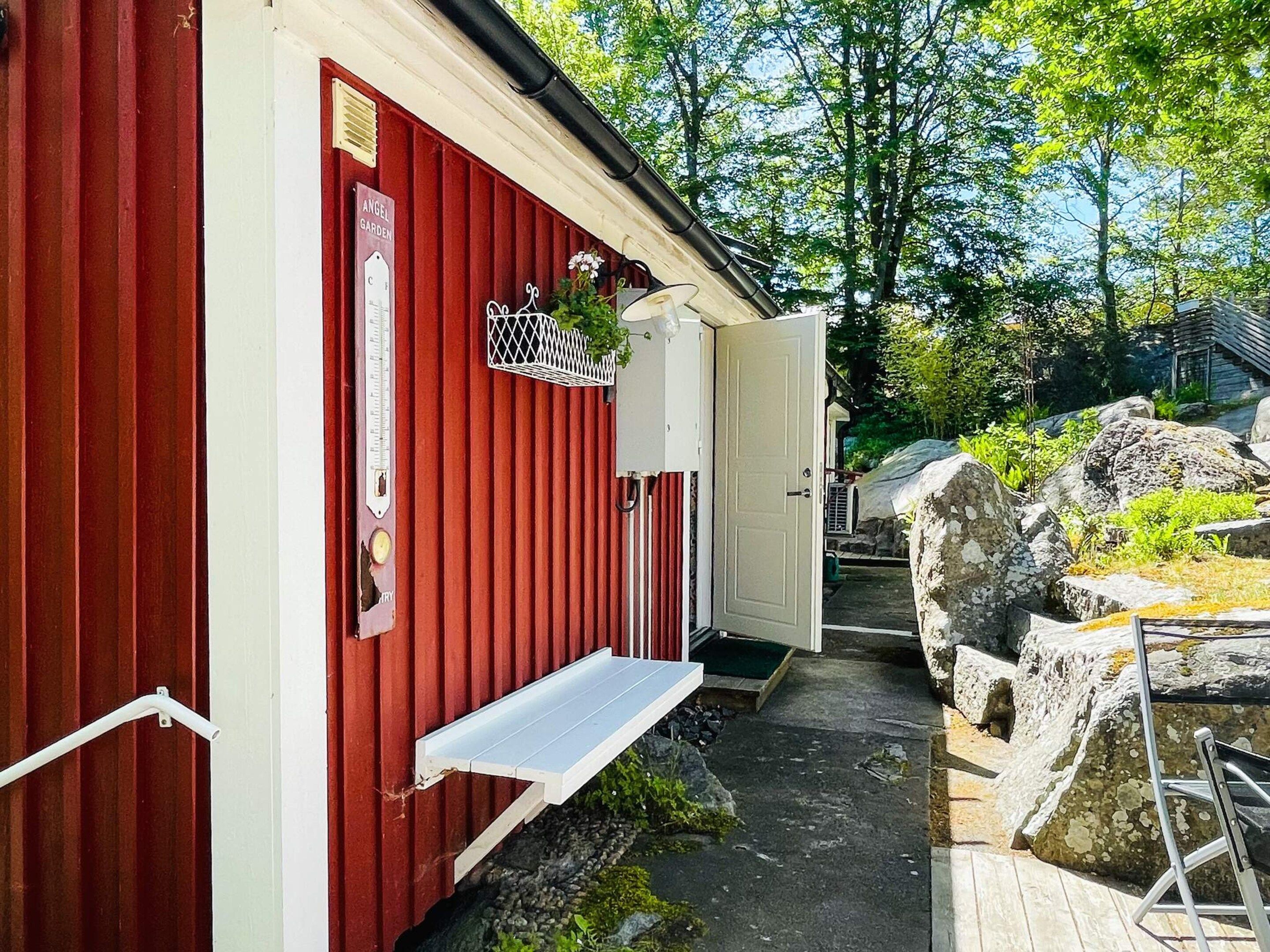 Un bâtiment rouge avec une porte blanche, un petit banc blanc et une enseigne sur laquelle on peut lire : « JARDIN D’ANGE ».