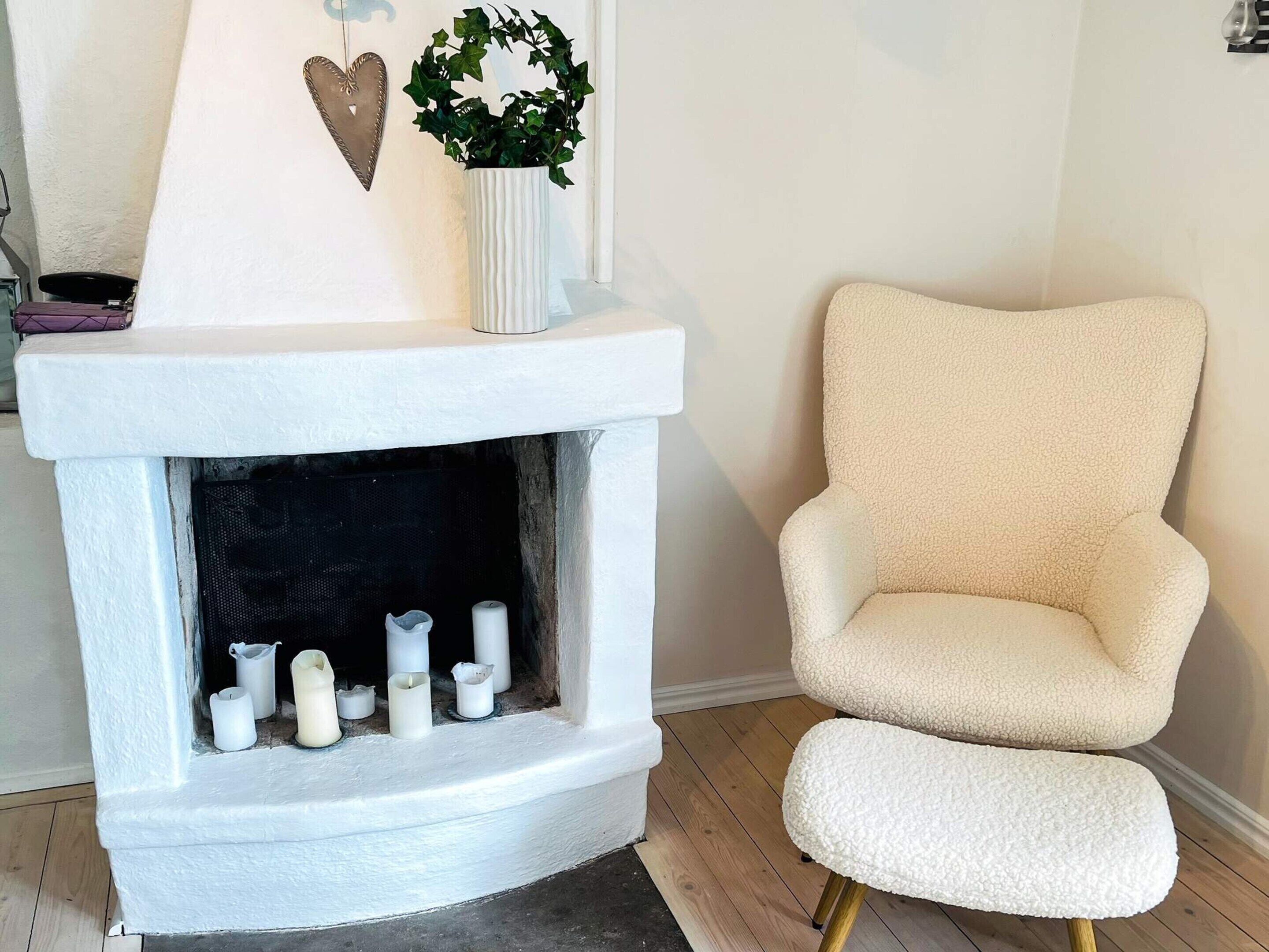 A white fireplace with a mantel, a white chair with a fluffy seat, and a potted plant.