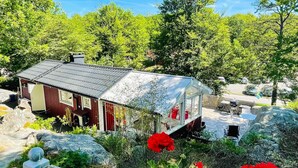 Uma cabana de madeira com telhado de metal, rodeada por vegetação e pedras grandes.