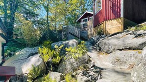 Uma cabana com exterior vermelho, cercada por pedras grandes e vegetação.