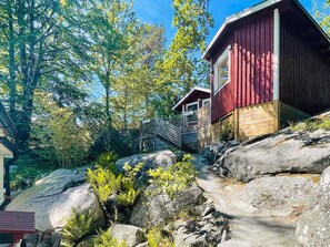 En hytte med rødt ydre, omgivet af store sten og grøn bevoksning.