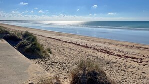 En strand med en gångstig av betong, en sandstrand och gles vegetation.