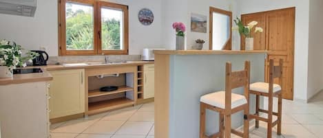 A modern kitchen with wooden cabinets, a built-in island with bar stools, a window with a view, and a wall clock.