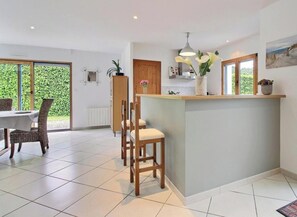 A modern kitchen with a central island, dining area with wicker chairs, and large windows. - Ty Ar Mor Bras - MERLEVENEZ (MERLEVENEZ)