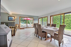 A dining area with a table set for six, surrounded by wicker chairs, and a view of a garden through large sliding glass doors. - Ty Ar Mor Bras - MERLEVENEZ (MERLEVENEZ)