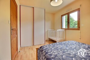 Een slaapkamer met een bed, een ledikant, een kast en een raam met uitzicht op groen.