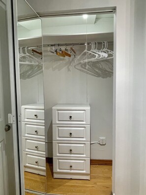 Ein begehbarer Kleiderschrank mit Spiegelüren, Holzboden und einem weißen Stauraumelement mit Schubladen.
