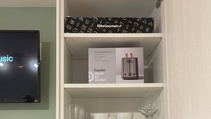 Een keuken met een magnetron, koffiezetapparaat, broodrooster en een televisie aan de muur.