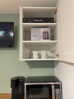 Eine Küche mit Mikrowelle, Kaffeemaschine, Toaster und einem an der Wand befestigten Fernseher.