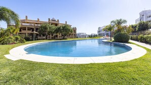 Une piscine entourée de pelouses et d’arbres bien entretenus, avec des bâtiments en arrière-plan.