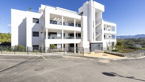 Un immeuble moderne à plusieurs étages, doté de balcons, d’un espace de stationnement et surplombant un paysage montagneux.