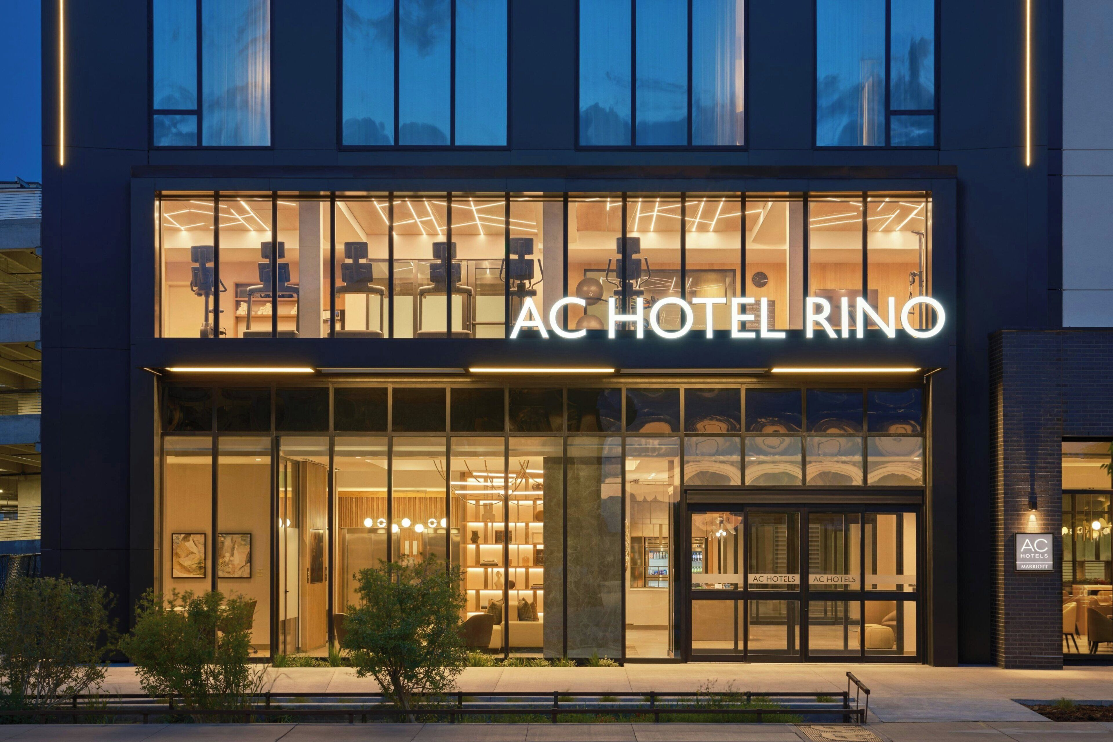 A hotel with a modern facade, large glass windows, and a prominent sign reading 'AC HOTEL RINO'.