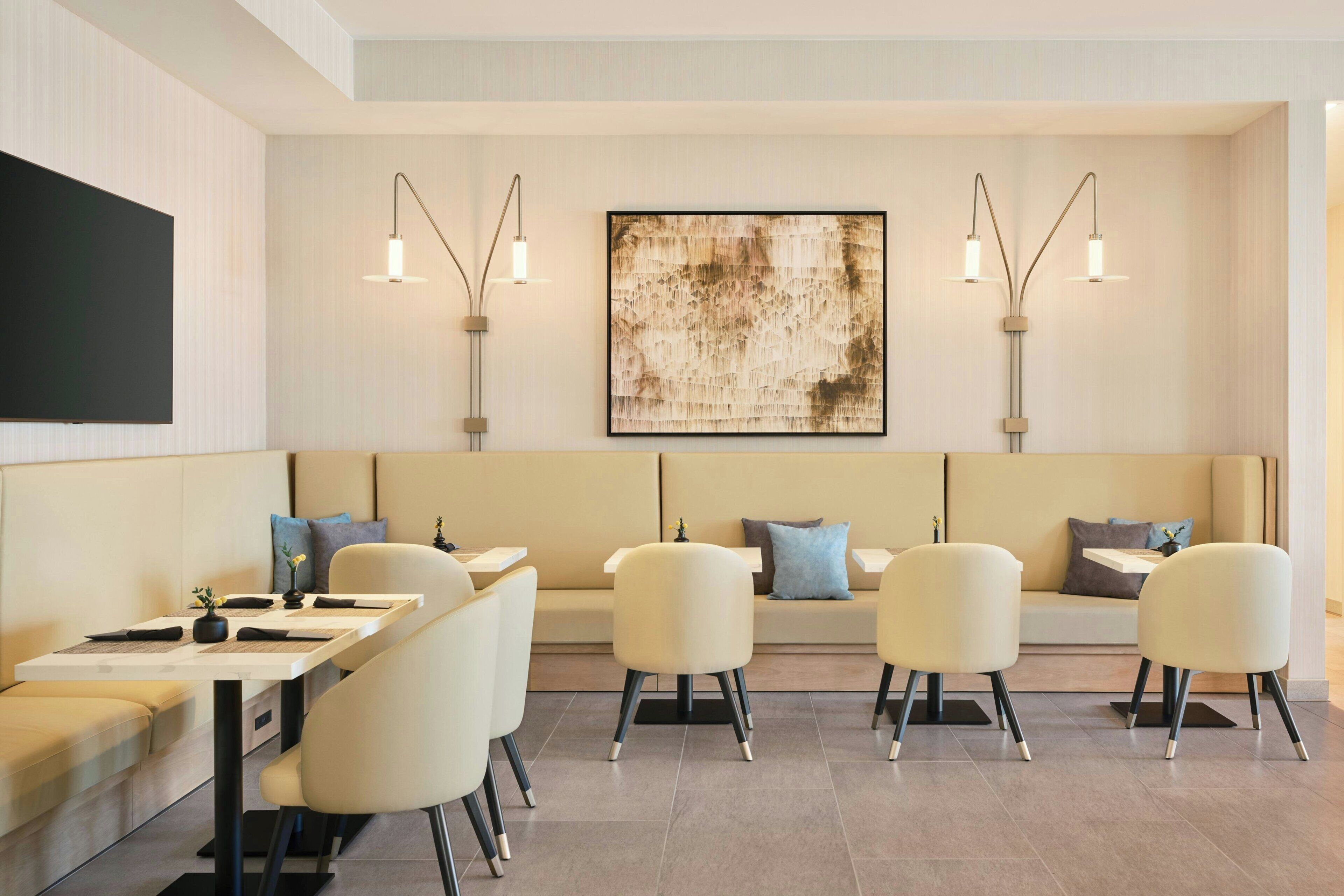 A modern hotel room with a dining area, a sofa set, and a large abstract painting on the wall.