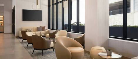 A modern hotel lobby with a sofa set, round tables, and a large TV screen.