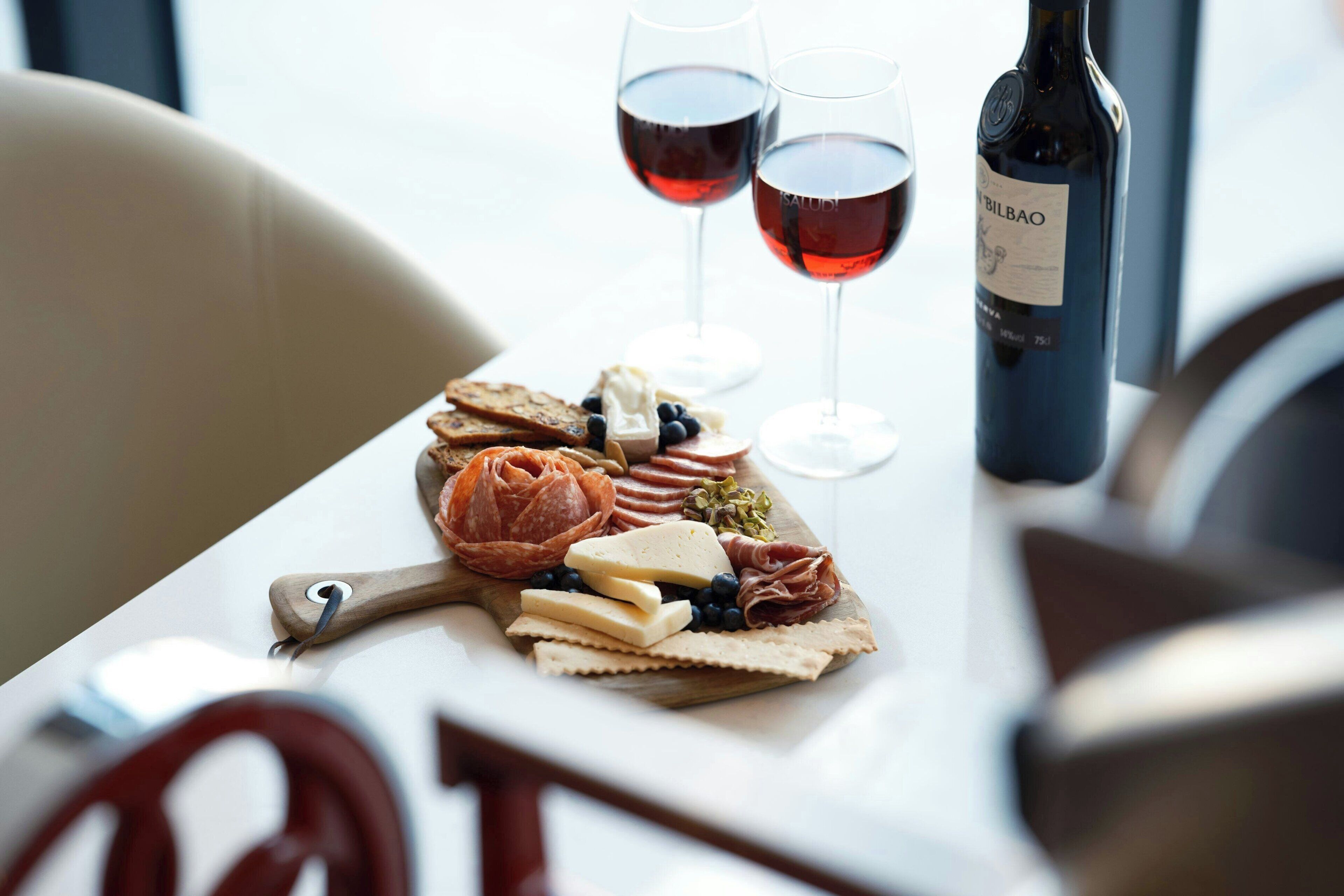 Una tabla de fiambres, dos copas de vino tinto y una botella de vino.