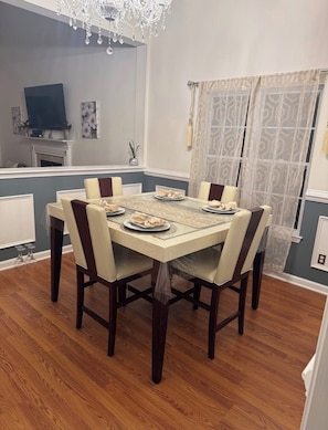 A dining area with a table set for six, surrounded by chairs, a chandelier, a television, and a patterned curtain.